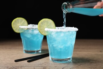 Bartender making cocktail with light blue drink at wooden table, closeup