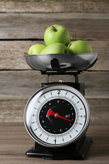 Kitchen scale with green apples on wooden table