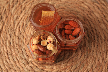 Jars with different nuts and honey on wicker mat, above view