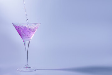 Pouring fresh cocktail into martini glass on light blue background, space for text