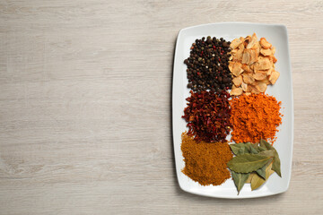 Plate with different spices on light table, top view. Space for text