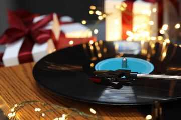 Turntable with vinyl record, fairy lights and Christmas gift boxes, closeup