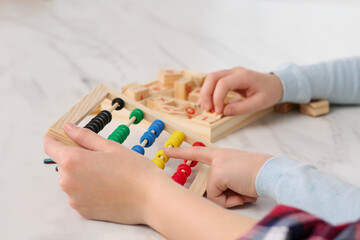 Mother and daughter playing with different math game kits at white marble table, closeup. Study...