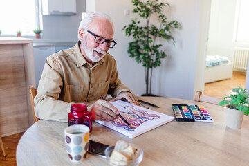 Elderly man is painting in her home. Retirement hobby.