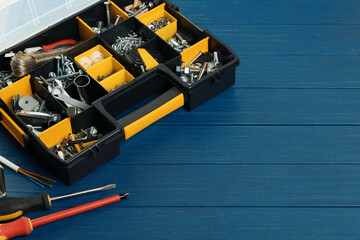 Plastic box with different furniture fittings and tools on blue wooden table, space for text