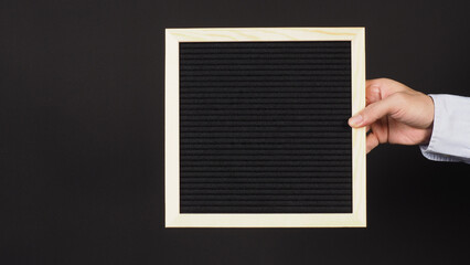 Hand is holding a black letter board on black background.