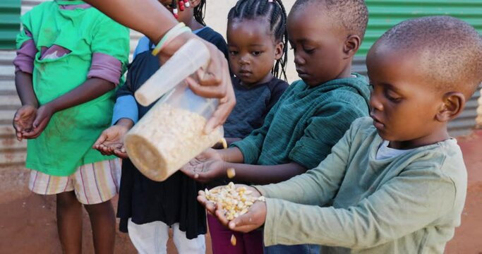 Poverty in Africa. Small group of starving Black African children holding their hands out while a charity organisation distributes corn