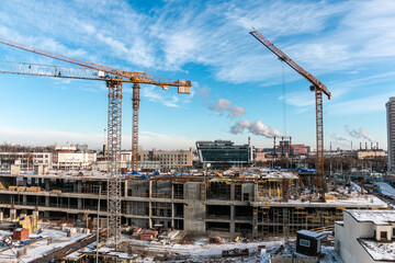 Fototapeta na wymiar Construction cranes at a construction site in the city against a blue sky in winter conditions. The concept of building a new area. Construction of a new building. The work of building cranes.
