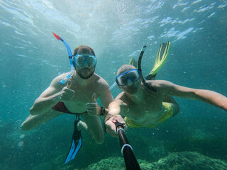 Underwater view of two joung friends snorkeling making  ok sign and taking a selfie. Snorkeling, holiday and summer concept - obrazy, fototapety, plakaty