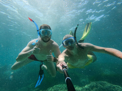 Underwater view of two joung friends snorkeling making  ok sign and taking a selfie. Snorkeling, holiday and summer concept