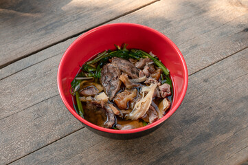 Combination beef and offal noodle soup with vegetable in red bowl on wooden table in local restaurant