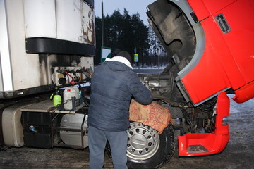 Truck driver repairs diesel engine under hood on truck head with refrigerator semi trailer