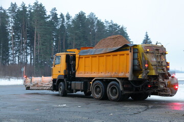 Heavy yellow dump truck with Snowplow scraper shovel blade and sand pile on winter highway road