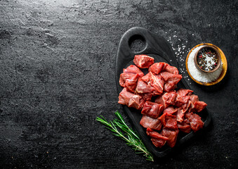 Cut raw beef on a black cutting Board with rosemary.