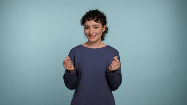 Portrait smiling curly woman rubbing fingers showing cash money gesture asking for give me money. Joyful female wearing blue sweater looks camera on isolated light blue background with copy space