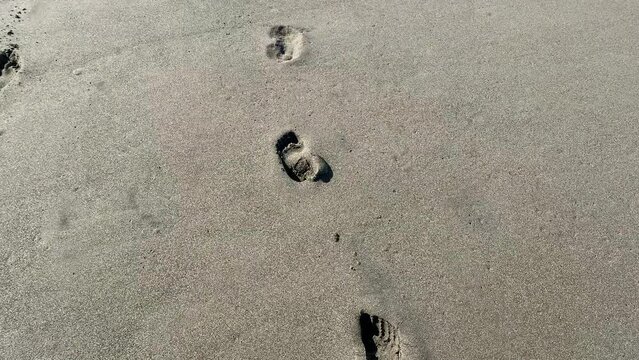 Footprints in the sand, washed away by the wave