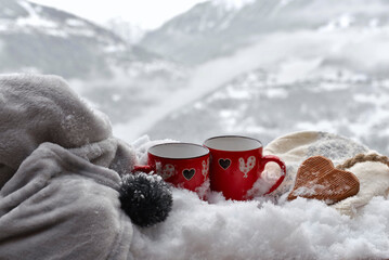 two red mugs withwooden  heart shaped on the snow with blanket on  mountain