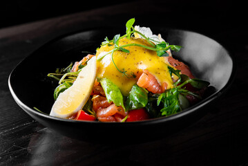 Salad with Boiled Eggs, Salmon, Tomatoes and cucumber in a bowl on black background