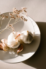 Organic Natural Garlic Cloves and dried flowers on plate in afternoon sunlight