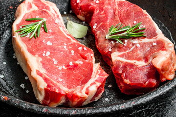 Raw beef steaks in an old pan with rosemary sprig.