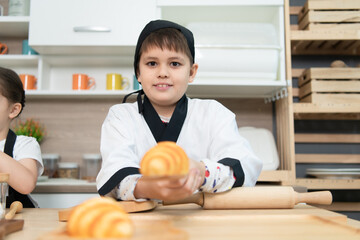 Fototapeta premium Portrait of a little boy in the kitchen of a house having fun playing baking bread