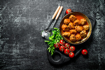 Meat balls in pan on a cutting Board with tomatoes and parsley.