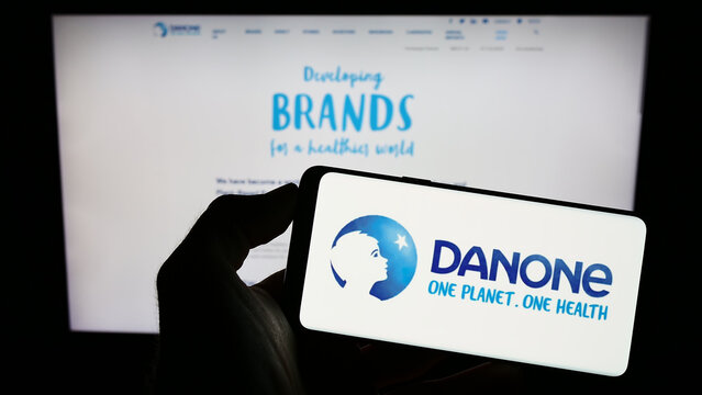 Stuttgart, Germany - 01-13-2023: Person holding smartphone with logo of French food company Danone S.A. on screen in front of website. Focus on phone display.