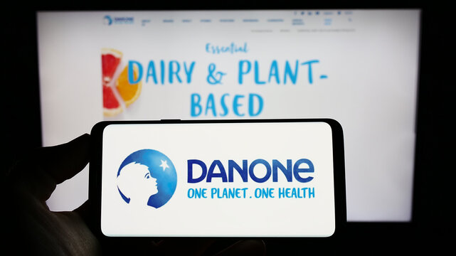 Stuttgart, Germany - 01-13-2023: Person holding cellphone with logo of French food company Danone SA on screen in front of business webpage. Focus on phone display.