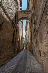 Narrow street between two medieval stone buildings joined by a stone and brick arch, in Italy - 562452200