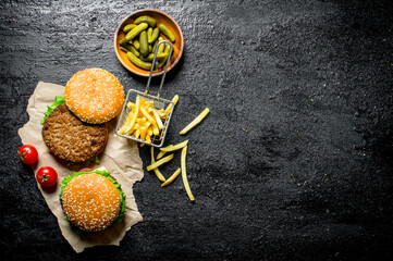 Burgers on paper with French fries, pickles and tomatoes.