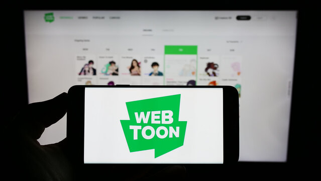 Stuttgart, Germany - 01-13-2023: Person holding cellphone with logo of digital comic company WEBTOON Entertainment Inc. on screen in front of webpage. Focus on phone display.