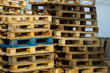 A stack of wooden pallets in an internal warehouse. An outdoor pallet storage area under the roof next to the store. Piles of Euro-type cargo pallets at a waste recycling facility.