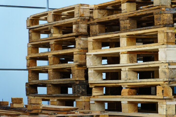 A stack of wooden pallets in an internal warehouse. An outdoor pallet storage area under the roof next to the store. Piles of Euro-type cargo pallets at a waste recycling facility.