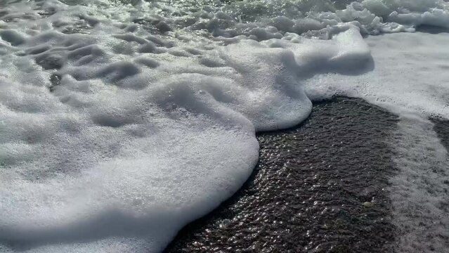 The sea wave with foam pours on the sandy shore
