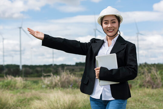 person  holding tablet.  Business holding tablet.  Asian woman in white helmet working with digital tablet at renewable energy farm. Female inspector controlling functioning of wind turbines outdoors.