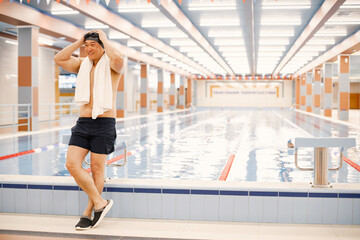 Fototapeta na wymiar Asian man standing in indoors swimming pool with a towel on his shoulders