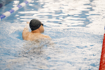 Man an in hat swimming in indoors swimming pool breaststroke