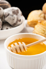 Liquid natural bee honey in a white ceramic bowl with a wooden spoon, with honey cookies and cocoa cookies.