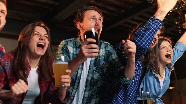 Goal. Group of young people, friends, emotionally watching match at pub. Fans cheering up favourite sport team. Winning game