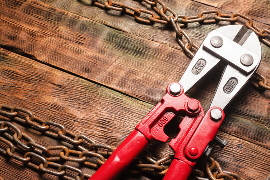 Bolt cutters rebar shears and iron chain on brown wooden workbench background. Top view.