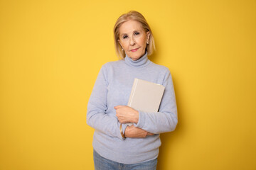 Photo of mature woman happy positive smile holding a book isolated over yellow background
