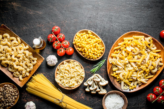 Assortment of different types of raw pasta with mushrooms, tomatoes and garlic.