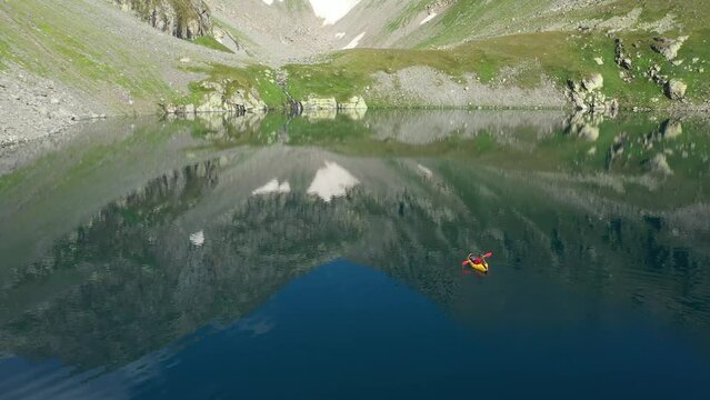 Woman Paddling on Packraft on Lake with Rocky Mountains Around. Aerial View
