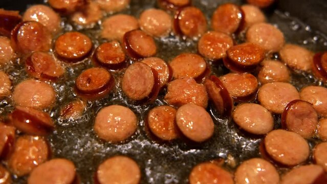 Slices of fried bangers in a frying pan. Farm, organic products. Homemade grilled pork barbecue sausages in an iron pan. Top view. Cooking Sausages. Roasted wurst, wiener. Full English breakfast. 4K