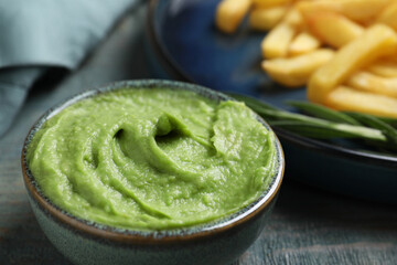Plate with delicious french fries, avocado dip and rosemary served on grey wooden table, closeup
