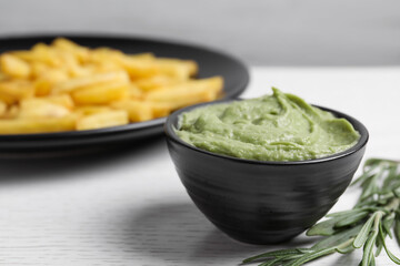 Dish with avocado dip, rosemary and plate of french fries on white wooden table, closeup