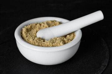 Mortar with mustard powder on black table, closeup