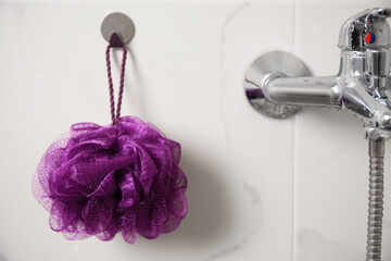 Purple shower puff hanging near faucet in bathroom