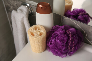 Purple shower puff, loofah sponge and bottle of body wash gel on sink in bathroom