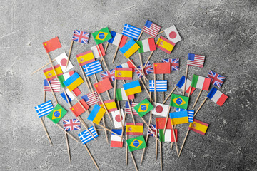 Many small paper flags of different countries on grey table, flat lay - obrazy, fototapety, plakaty